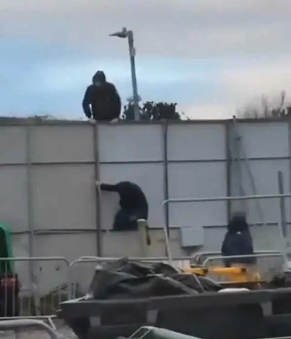 Is féidir líon beag fir le cochall (hooded men) a fheiceáil ag dreapadh thar bhacainní 