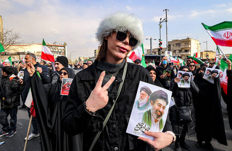 Bean ag seasamh le pictiúr de Cheannaire Uachtarach nua na hIaráine, an tAyatollah Mojtaba Khamenei (ar dheis), in aice lena athair nach maireann, Ali Khamenei. Oifig: mAtta KENARE/AFP via Getty Images