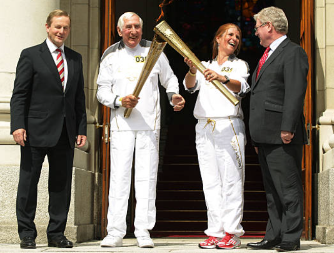 Ronnie ag tabhairt an Lasair Oilimpigh do Bridget Taylor agus iad ina seasamh leis an Taoiseach Enda Kenny agus an Tánaiste, le linn Sealaíocht Tóirse Oilimpeach Chluichí Oilimpeacha Londain i 2012, 2012 i mBaile Átha Cliath Pictiúr: LOCOG via Getty Images